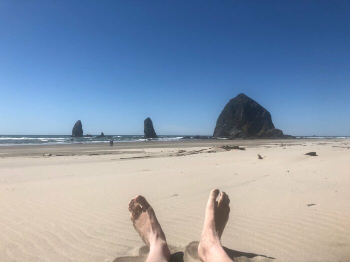 Fötter i sanden framför Haystack Rock